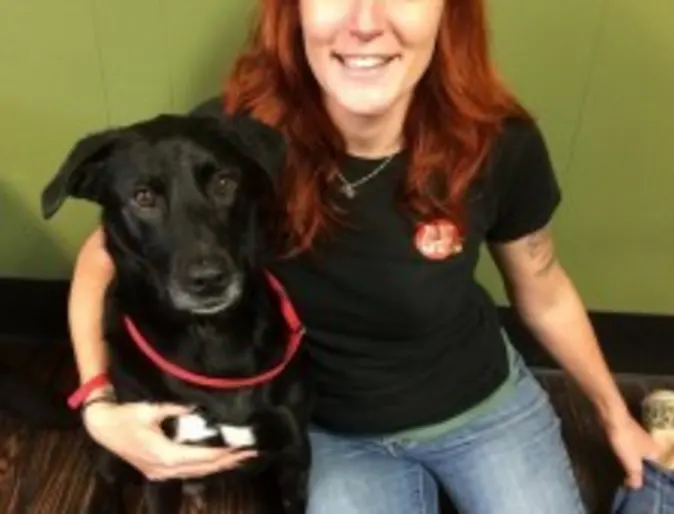 a red-haired woman sits on the floor with a black dog